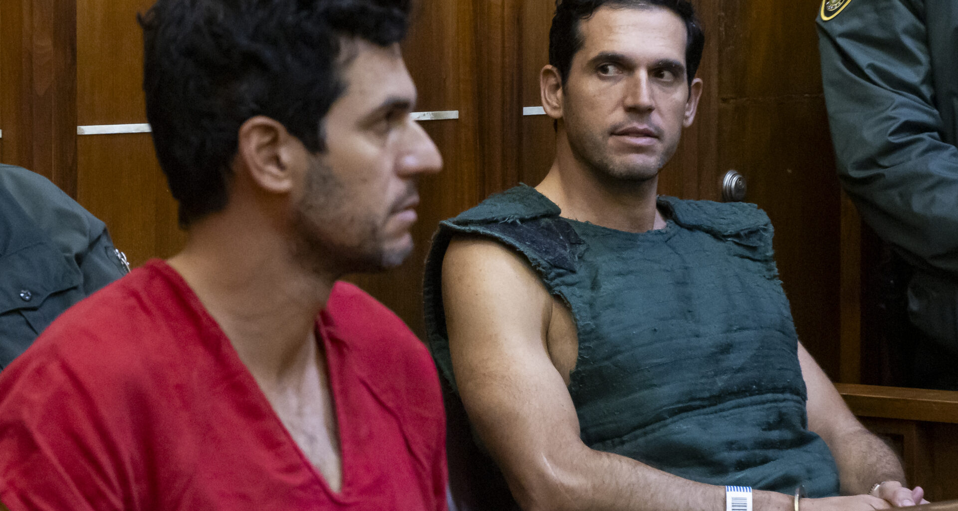 photo of a man in a red jumpsuit and another man wearing a navy kevlar vest inside a court room.