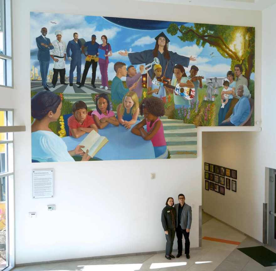Heights Foundation CEO Kathryn Kelly poses with muralist Juan Diaz beneath "The Growth of Our Beloved Neighborhood" in lobby of Education Building.