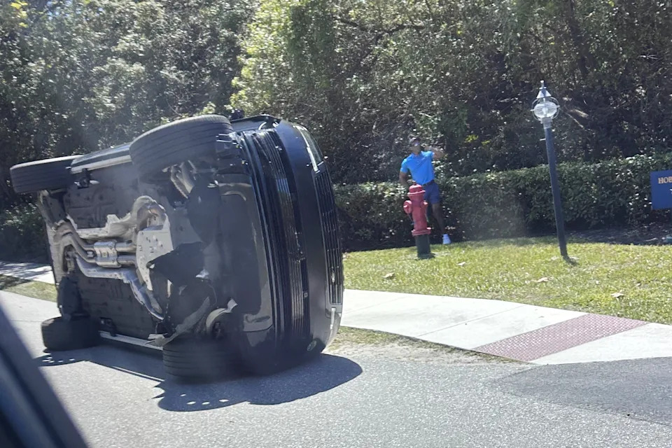 Golfer Tiger Woods stands by his overturned vehicle in Jupiter Island, Fla., on Friday, March 27, 2026. (AP Photo/Jason Oteri)