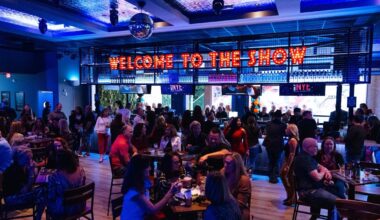 a packed bar with blue lighting and a neon sign