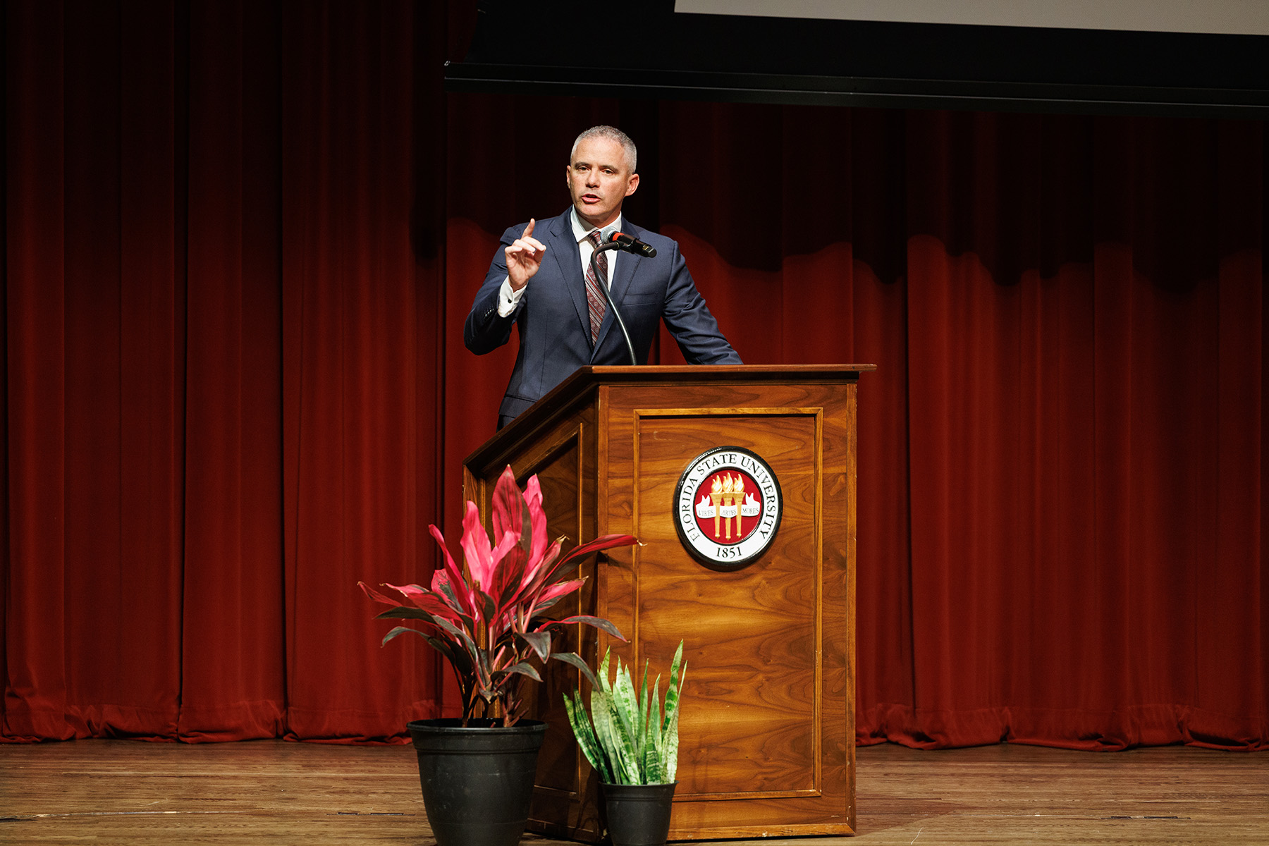 Head Football Coach Mike Norvell deliver remarks on stage in front of a podium