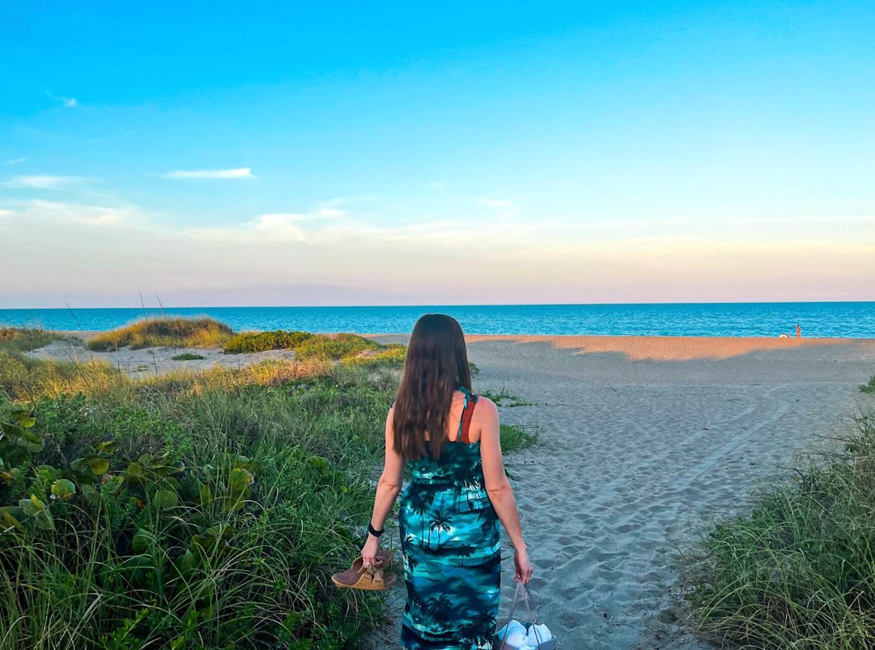 The writer carrying her shoes and a bag onto a quiet beach in Fort Pierce, Florida.