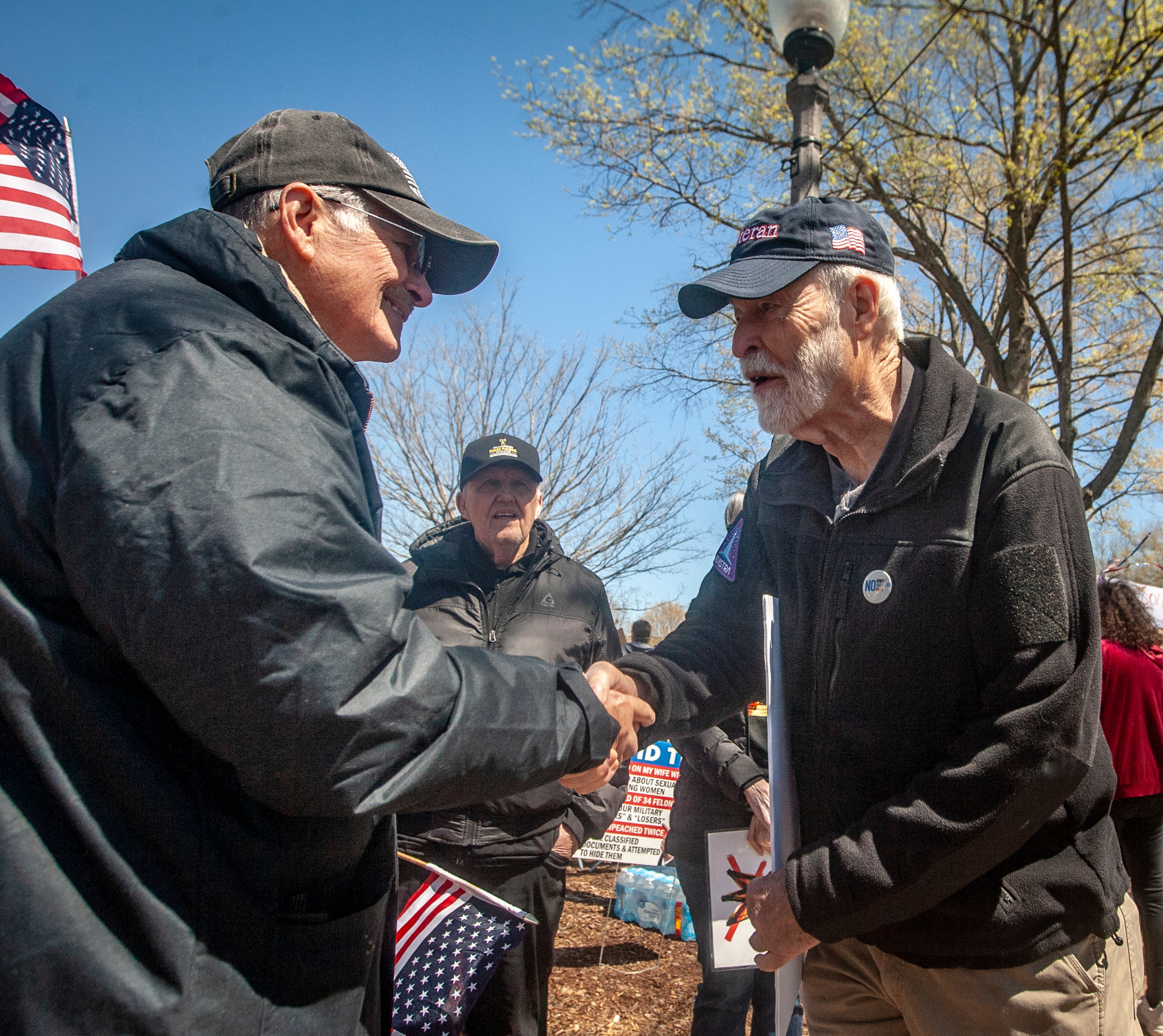 Two men shake hands while a third looks on. 