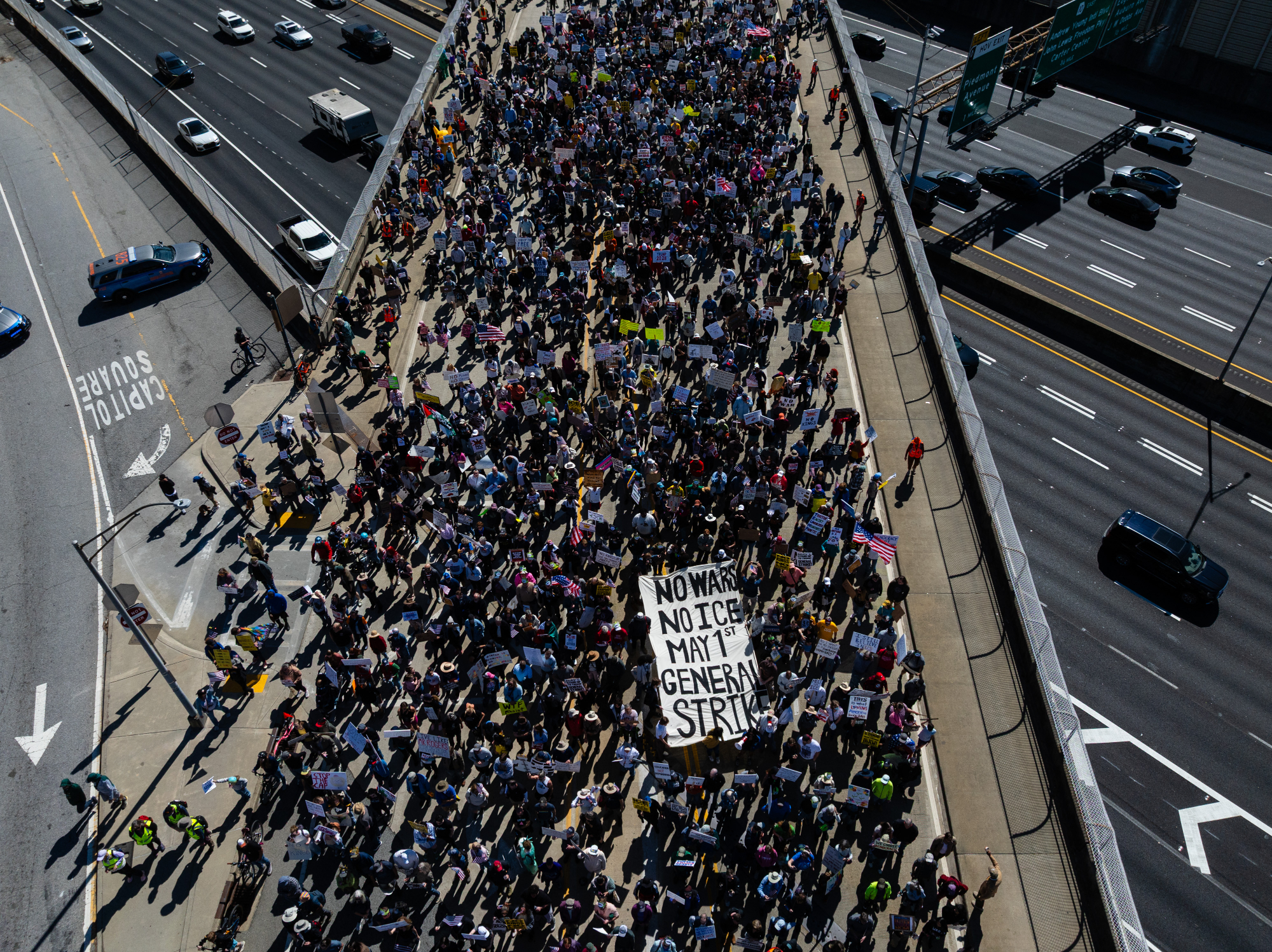 Protestors walk over a highway with a sign: "No wars. no ice. may 1st general strike."
