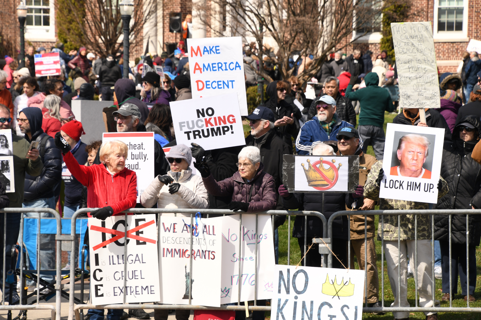 Miscellaneous signs are seen as people stand behind a barricade.  