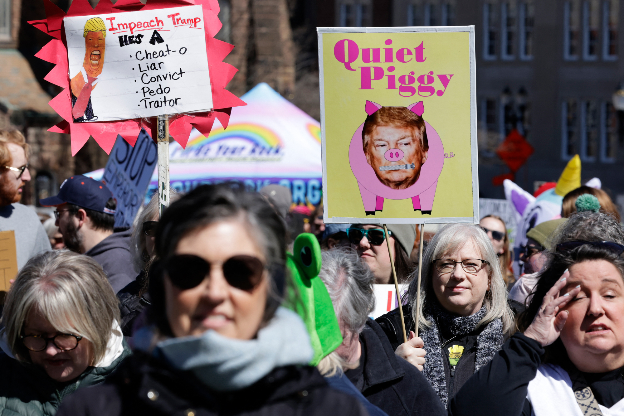 A sign reads: QUIET PIGGY with Trump's face on it. 