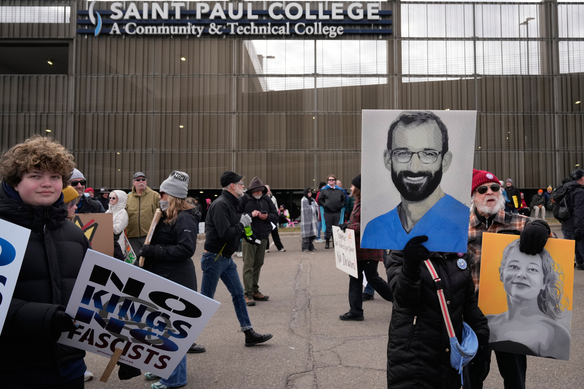 a protestor holds up photos of Renée Good and Alex Pretti.