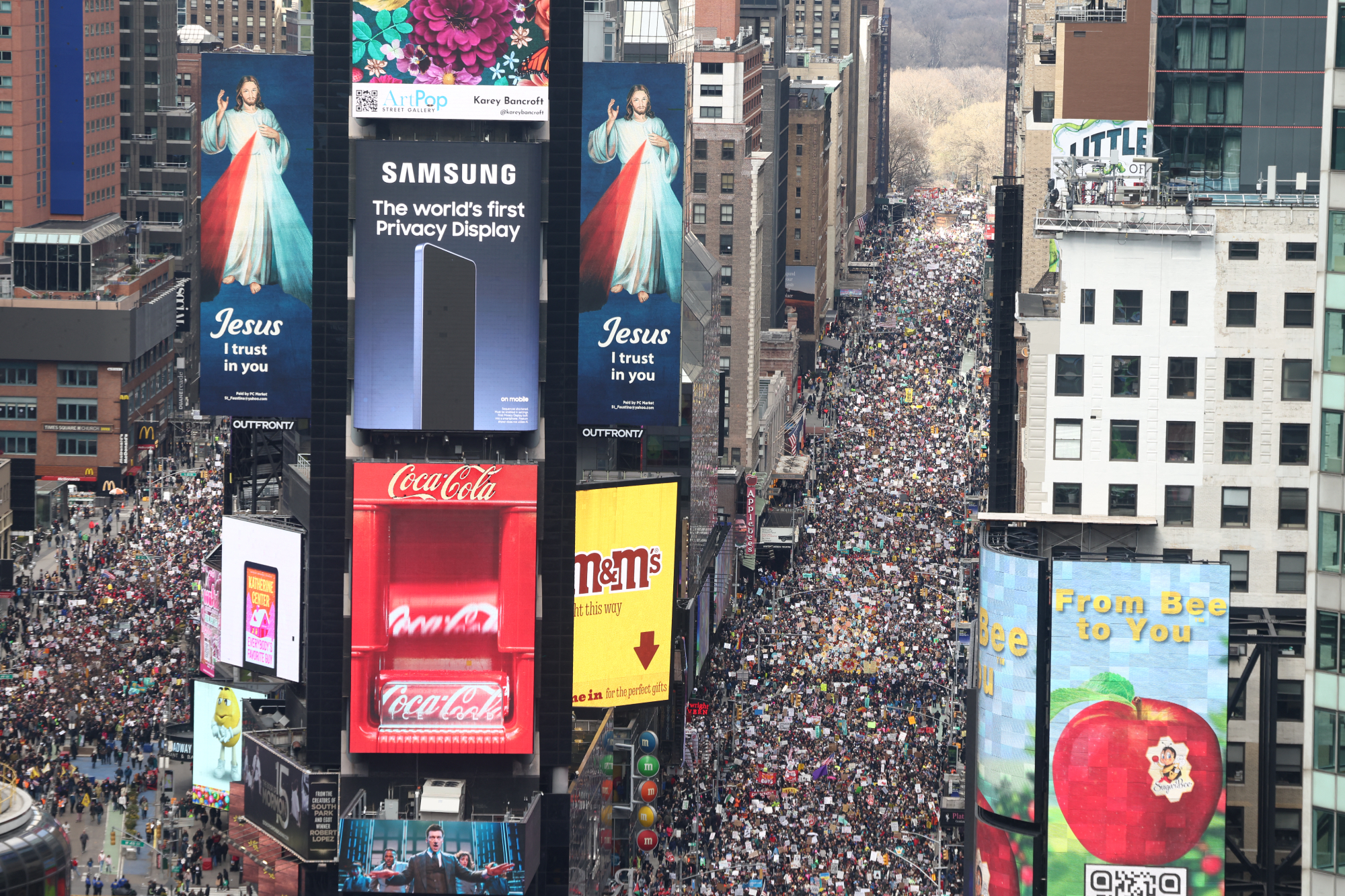 Times Square from above, filled with people. A Jesus advertisement is on the big screens. 