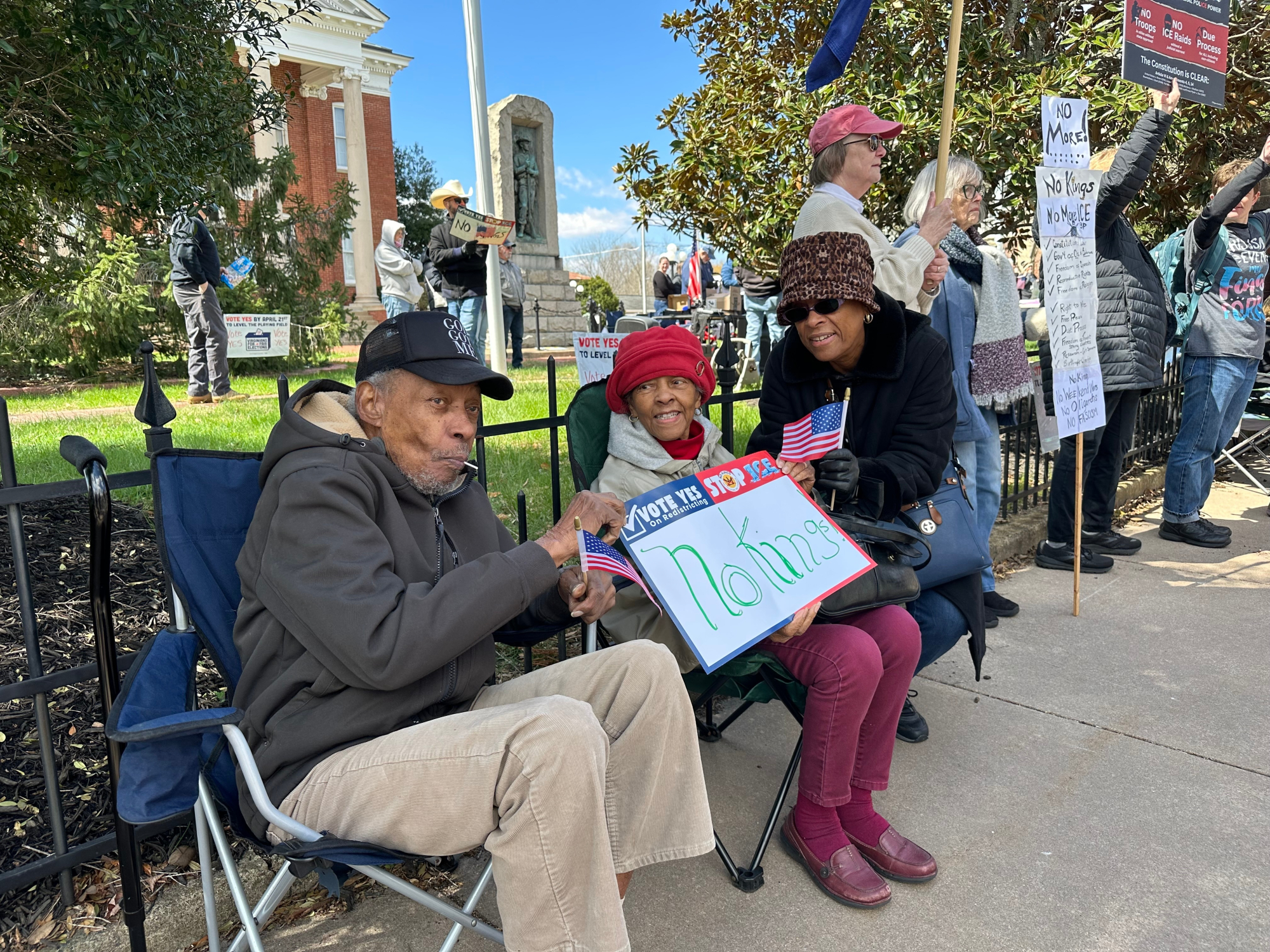 Protestors sit down in lawn chairs with a No Kings sign. 