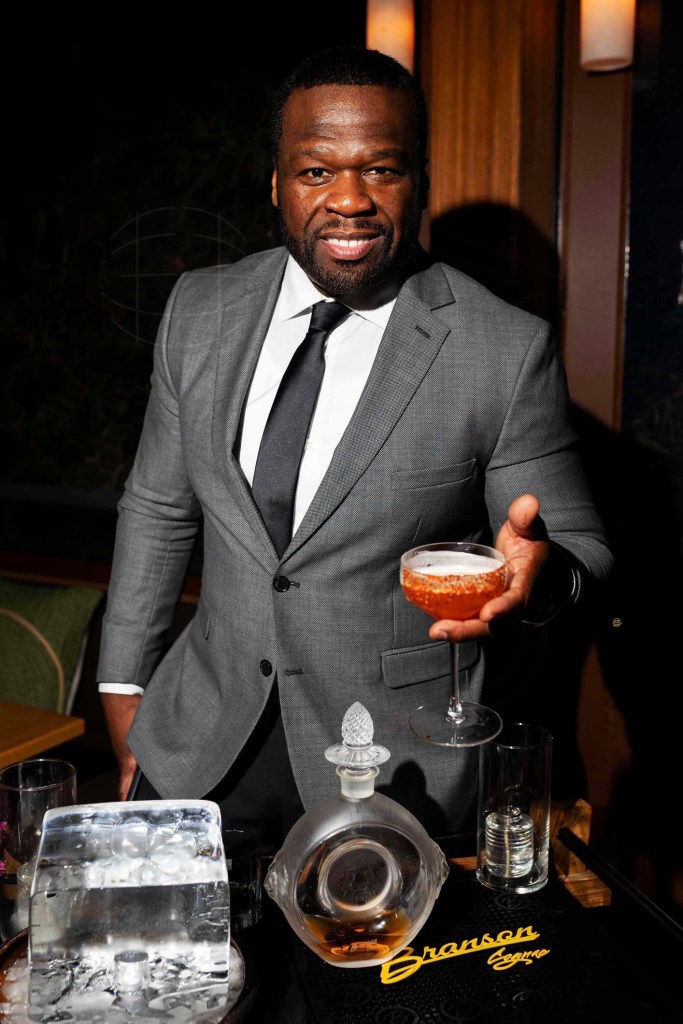 photo of rapper 50 cent in a suit and tie, posing while holding a red cocktail with tajin on the rim