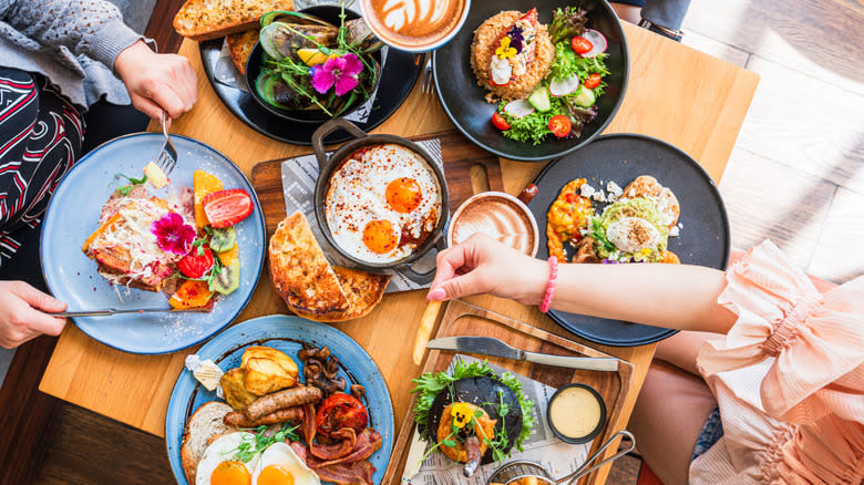 A display of brunch plates on a table with people's hands picking at them
