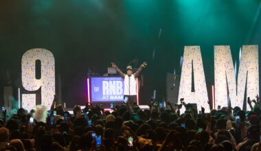 Photo of a man on stage in front of a crowd. The stage has letters that read 9am .