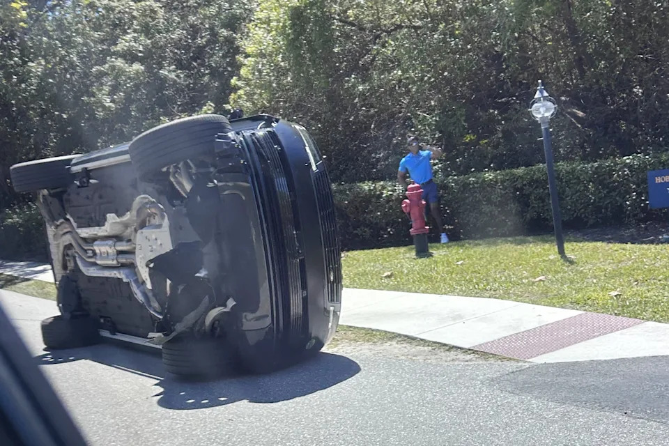 Golfer Tiger Woods stands by his overturned vehicle in Jupiter Island, Fla., on Friday, March 27, 2026. (AP Photo/Jason Oteri)