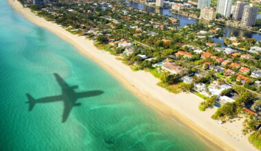 aerial photo of the shadow of a plane flying over the ocean in the direction of trees, houses, and skyscrapers in Miami