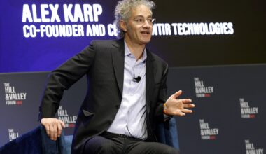 Alex Karp slightly sitting out of his chair while speaking at a panel