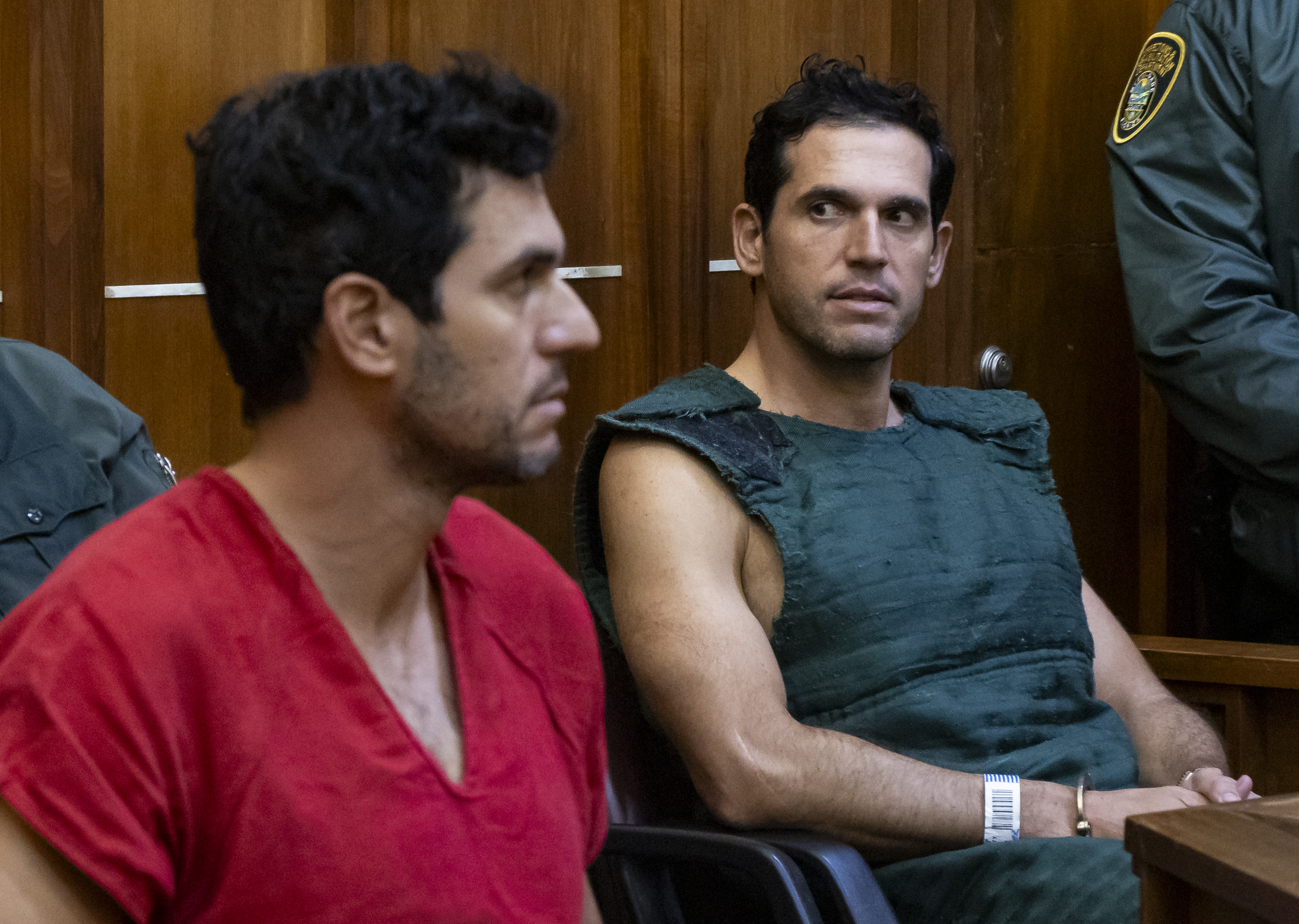 photo of a man in a red jumpsuit and another man wearing a navy kevlar vest inside a court room.