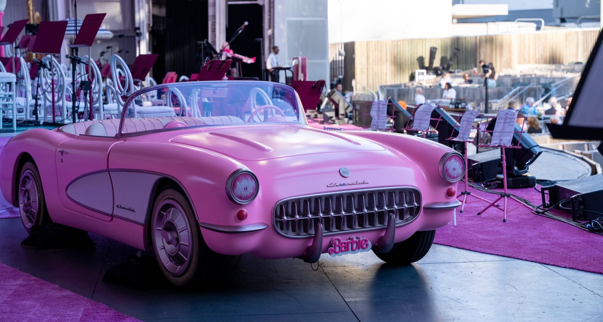 photo of a model pink convertible with a "Barbie" plate on an outdoor stage next to pink carpet and pink music stands
