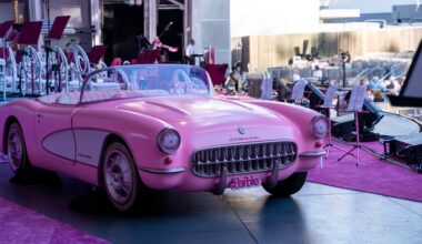 photo of a model pink convertible with a "Barbie" plate on an outdoor stage next to pink carpet and pink music stands