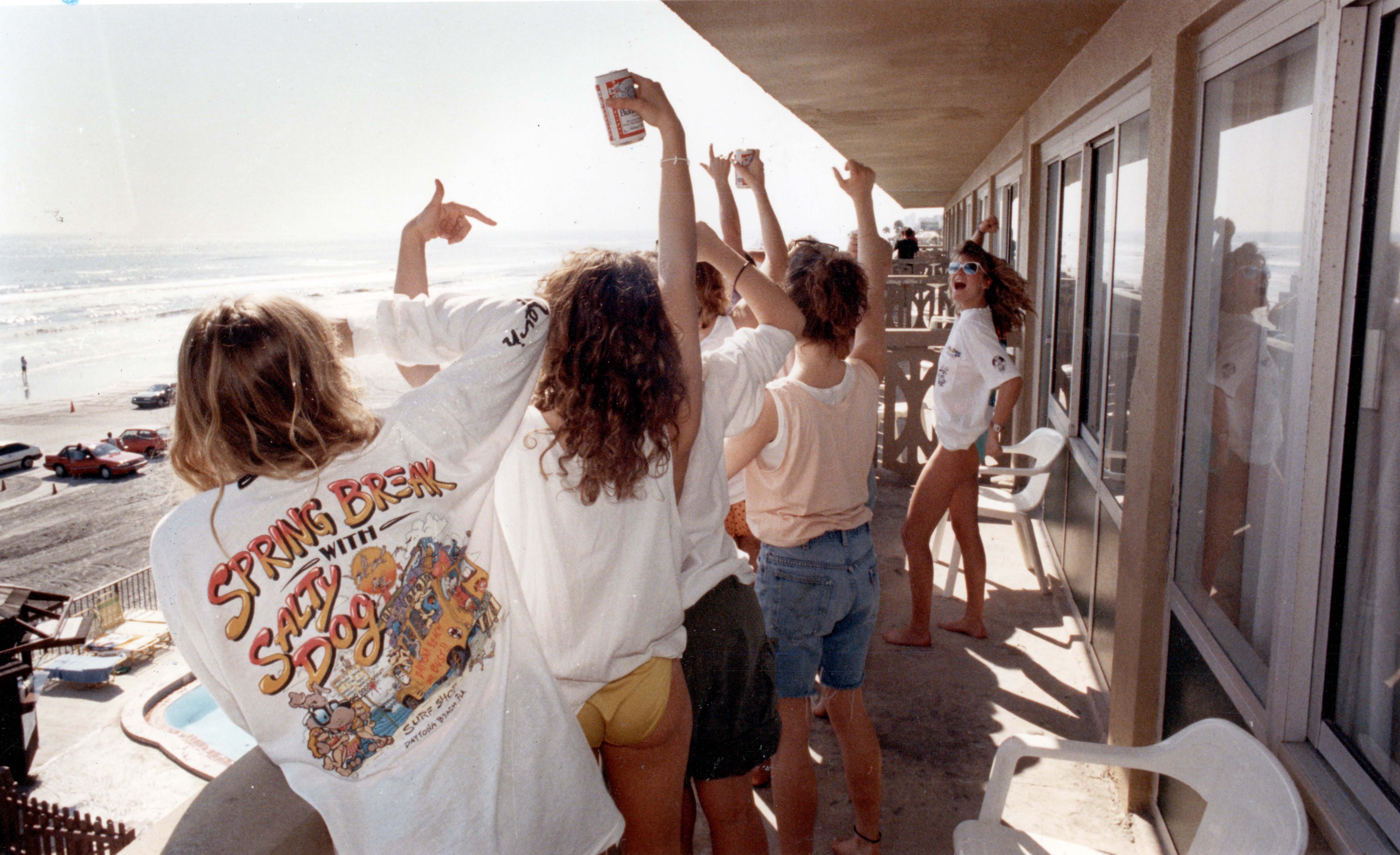 Female beachgoers cheer and yell from a hotel balcony to...