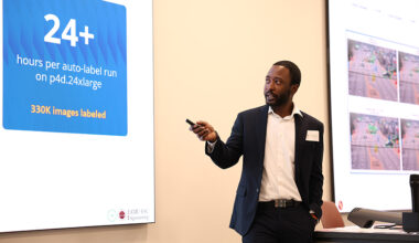 A man standing at a lectern gives a presentation. The screen behind him reads “24+ hours per auto-label run on p4d.24xlarge. 330K images labeled.”