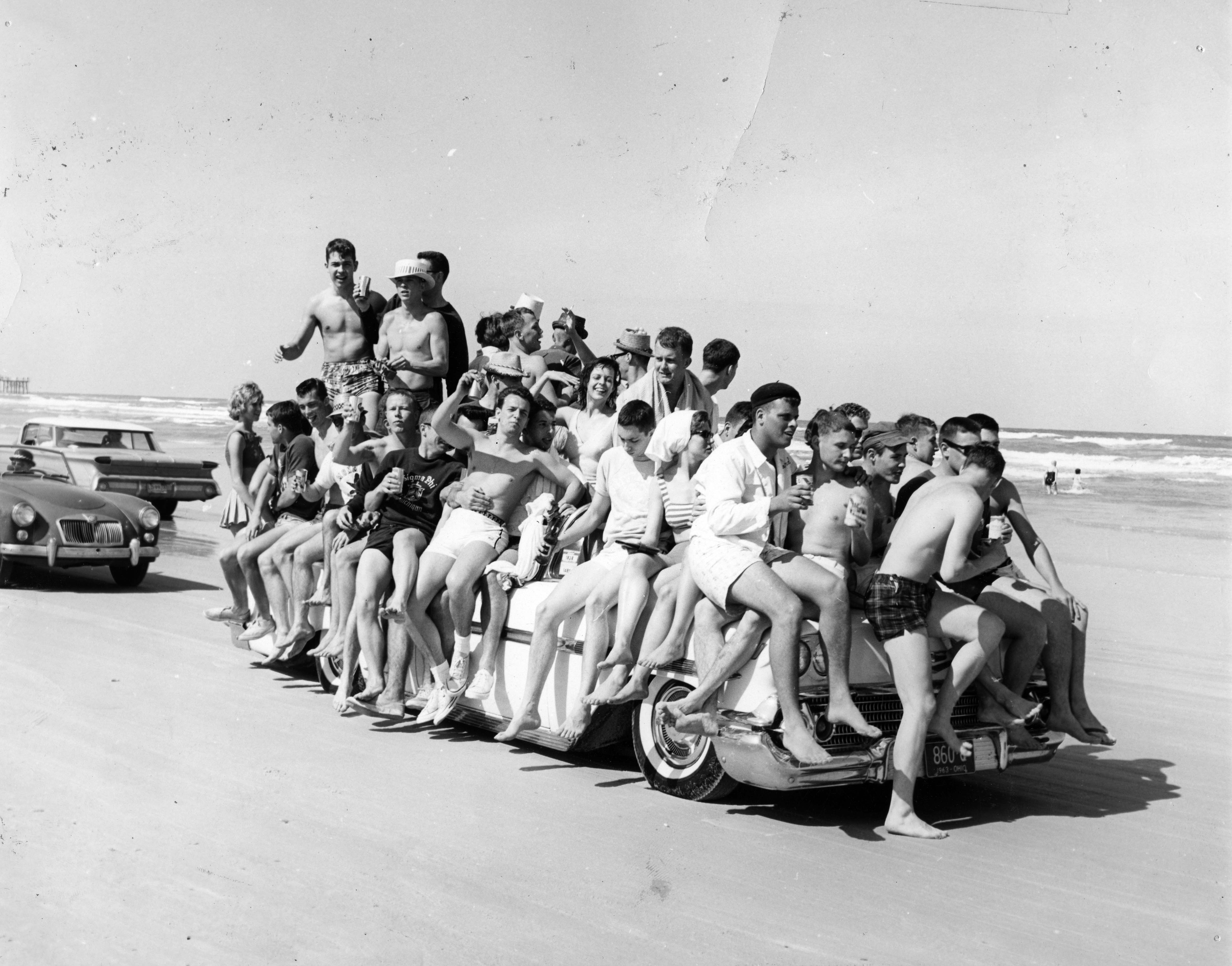 A large crowd of beachgoers pile on a vehicle driving...