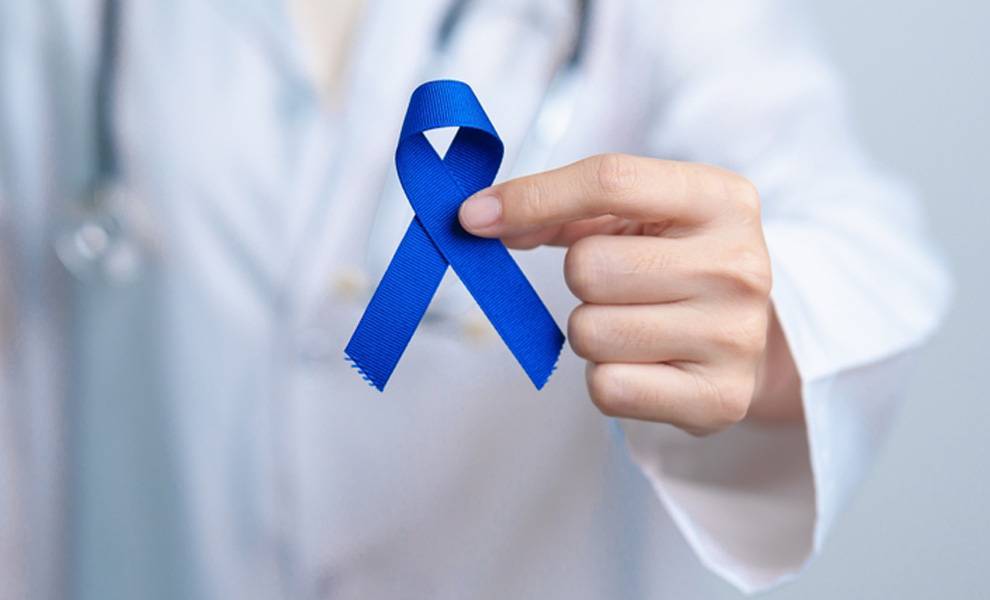 Care Resource Little Havana promotes weight management and colorectal cancer awareness 2 Close-up of a healthcare professional wearing a white coat holding a blue colorectal cancer awareness ribbon between their fingers.