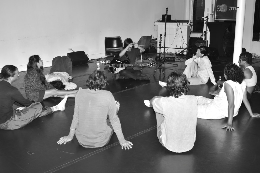 Photo of a group of people sitting on the floor next to someone playing guitar