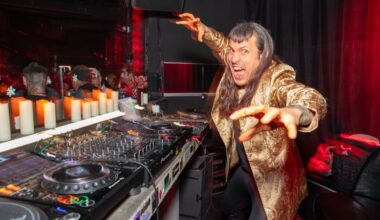 Photo of a man next to CDjs wearing a golden coat.