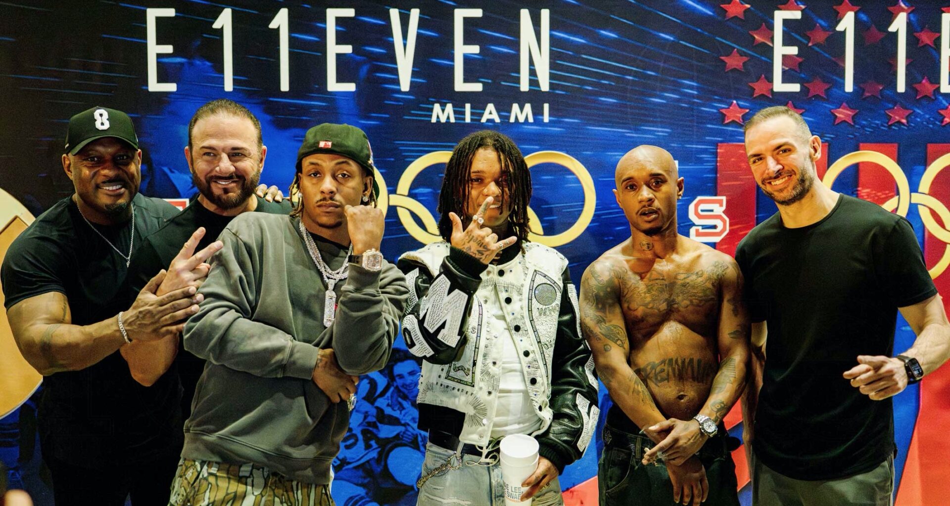 photo of six men posing together in front of a step-and-repeat showing a logo for E11even Miami