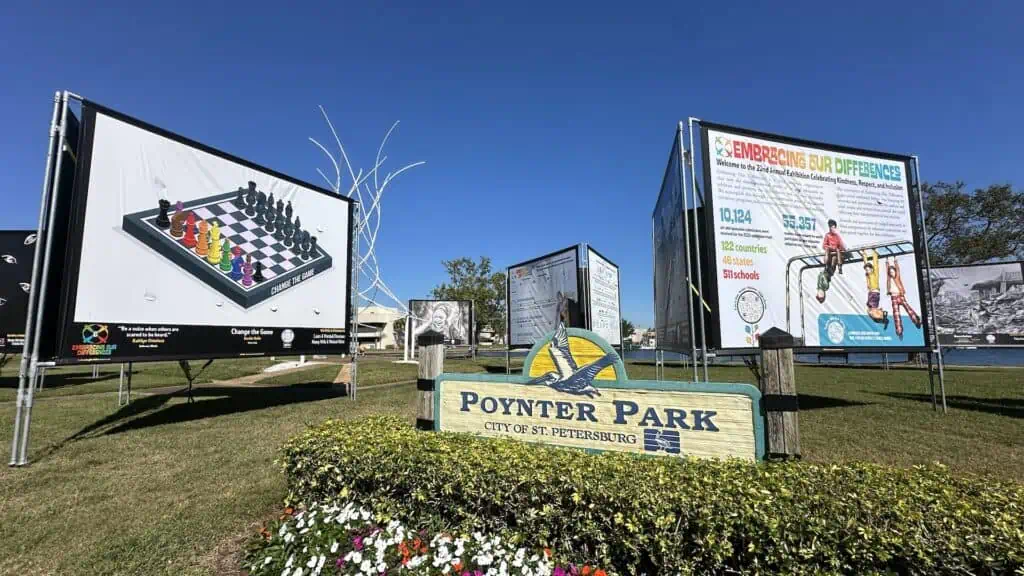 a park during the day with large paintings displayed on poles. A sign reads "Poynter Park"