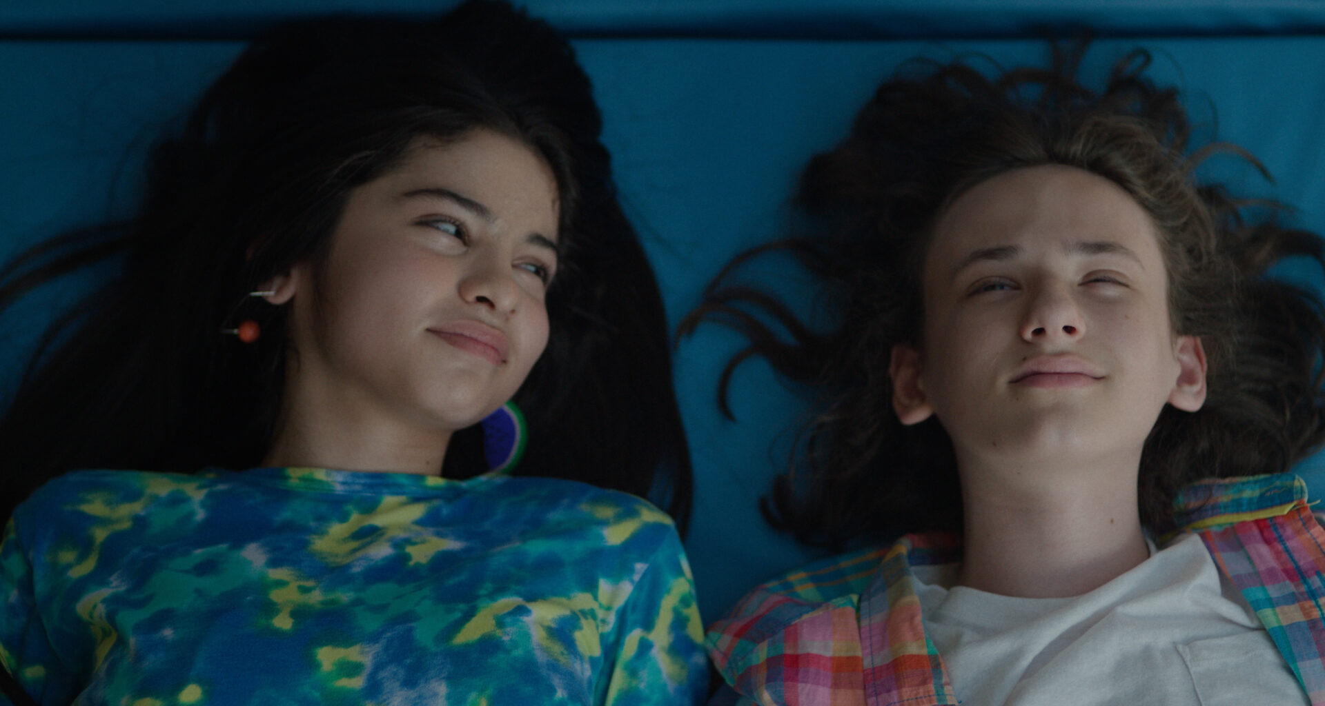 Still from the film 'Ethan Bloom' showing an overhead view of a young boy and older girl lying down. The boy looks up at the sky and the girl looks at the boy