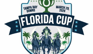 Badge logo for the 2026 Florida Cup at Tampa Bay Downs. The badge consists of a trophy centered at its top, with a horseshoe overlaid on top of the cup and “Tampa Bay Downs,” “March 29, 2026,” flanking its left and right sides respectively. There’s a ribbon cutting across the center of the badge that reads, “Florida Cup,” in all capital letters, and an illustration of three horses galloping beneath the ribbon.