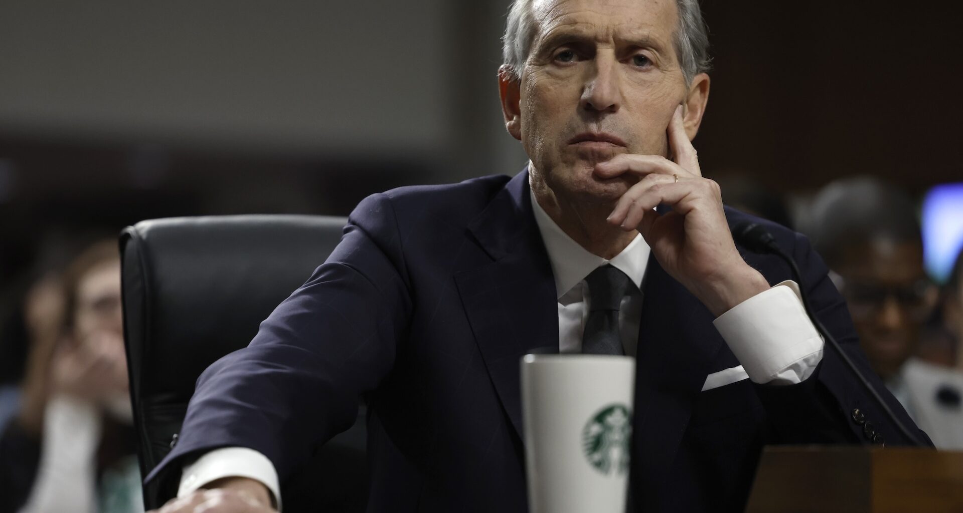photo of Starbucks CEO testifying in front of a senate committee on Capitol Hill. An out-of-focus Starbucks thermos is in front of him on the desk.