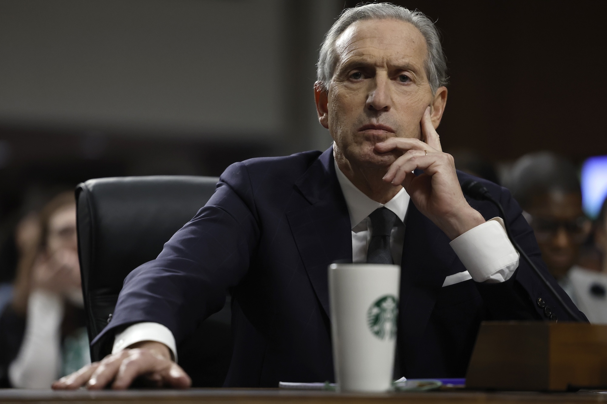 photo of Starbucks CEO testifying in front of a senate committee on Capitol Hill. An out-of-focus Starbucks thermos is in front of him on the desk.