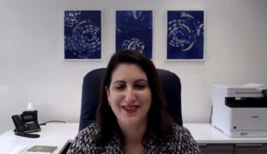 Angela Falconetti, a woman with long brown hair, sits at a chair and smiles.