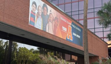 A sign with a red brick wall behind it shows five smiling students and a message that Orange County Public Schools got an A grade from state of FL.