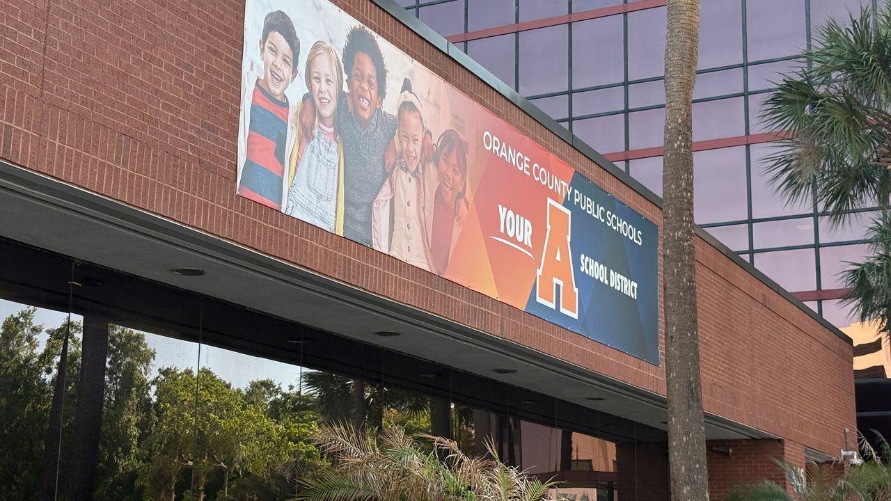 A sign with a red brick wall behind it shows five smiling students and a message that Orange County Public Schools got an A grade from state of FL.