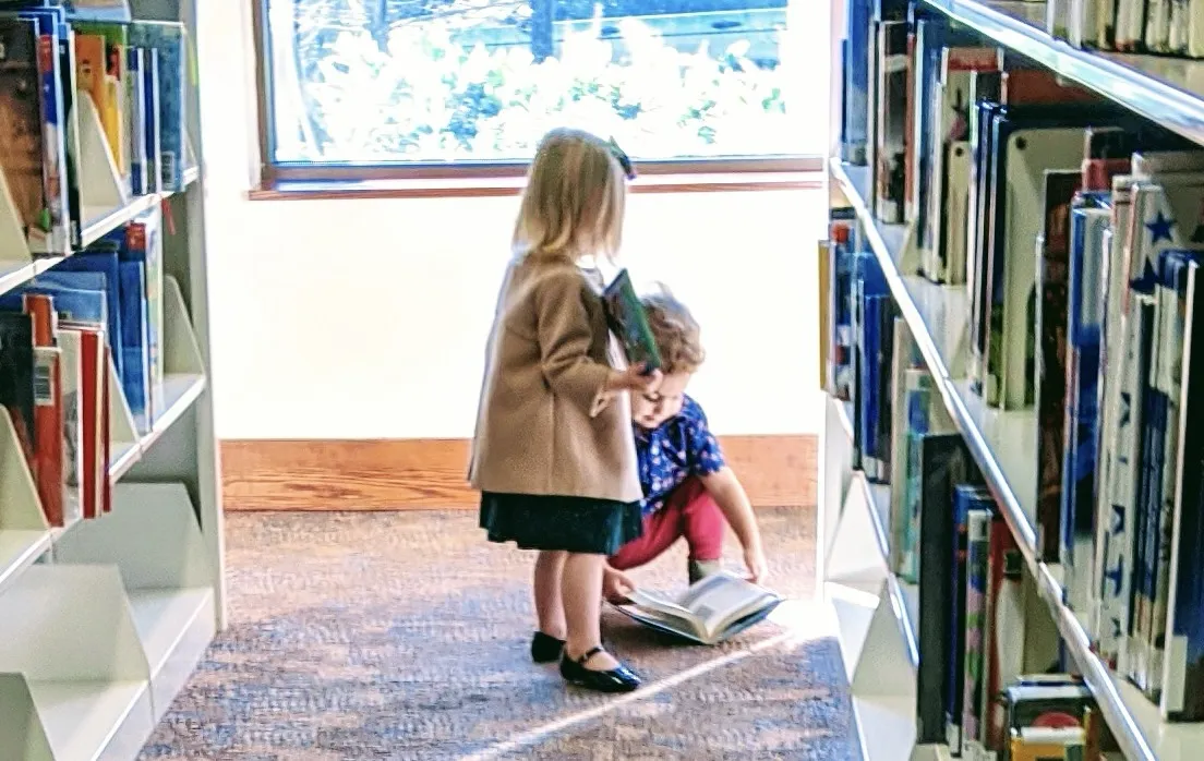 Two children stand among stacks of books