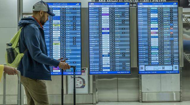 An information monitor shows departing and arriving flights with no cancellations at Miami International Airport on Friday, March 20, 2026, as a partial government shutdown causes TSA worker shortages and leads to long security lines nationwide.
