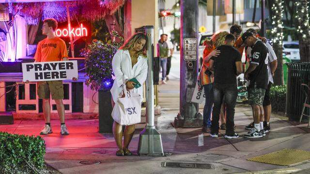 A woman waits to cross Ocean Drive as a group prays with the God Squad, an interfaith prayer team of volunteers for the Miami Beach Police Department who serve as goodwill ambassadors during spring break in the South Beach neighborhood of Miami Beach Florida on Friday, March 20, 2026.