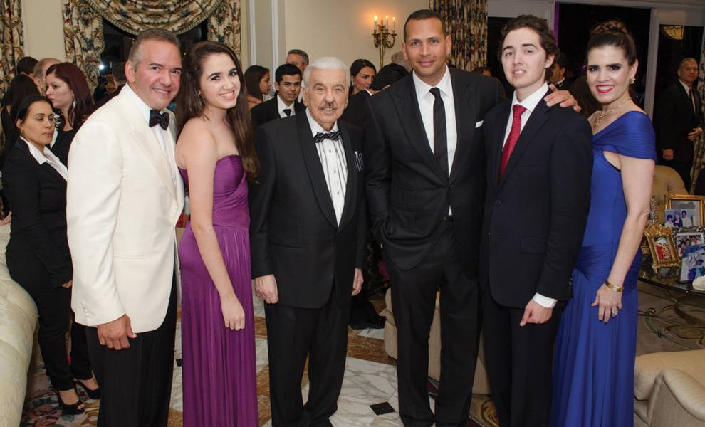 Honoring José Milton: A visionary who helped build South Florida and the communities within it 3 Jose Milton in a tuxedo stands at the center of a group at an indoor formal gathering, surrounded by well-dressed family members and guests in evening attire, smiling for a photo.