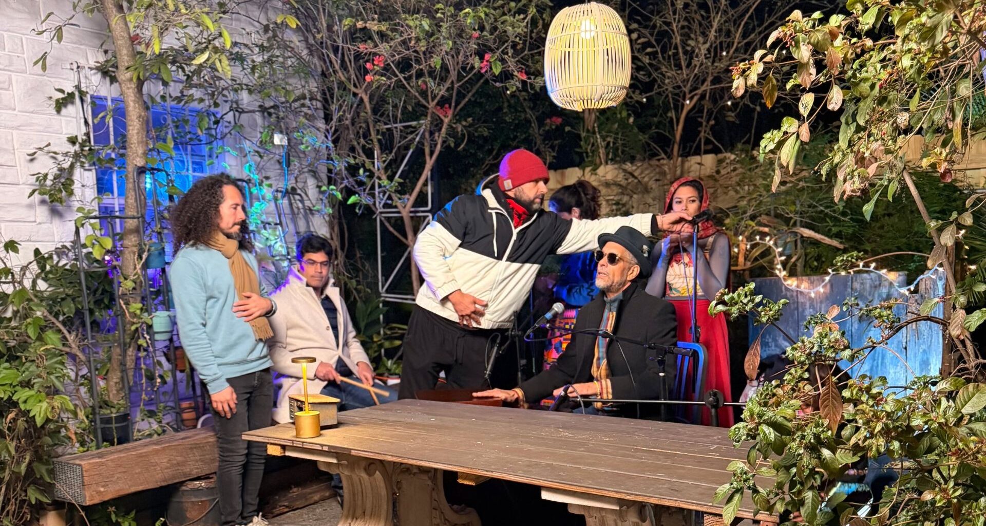 Photo of a band sitting by a table in a patio and a man holding a microphone