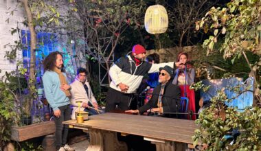 Photo of a band sitting by a table in a patio and a man holding a microphone