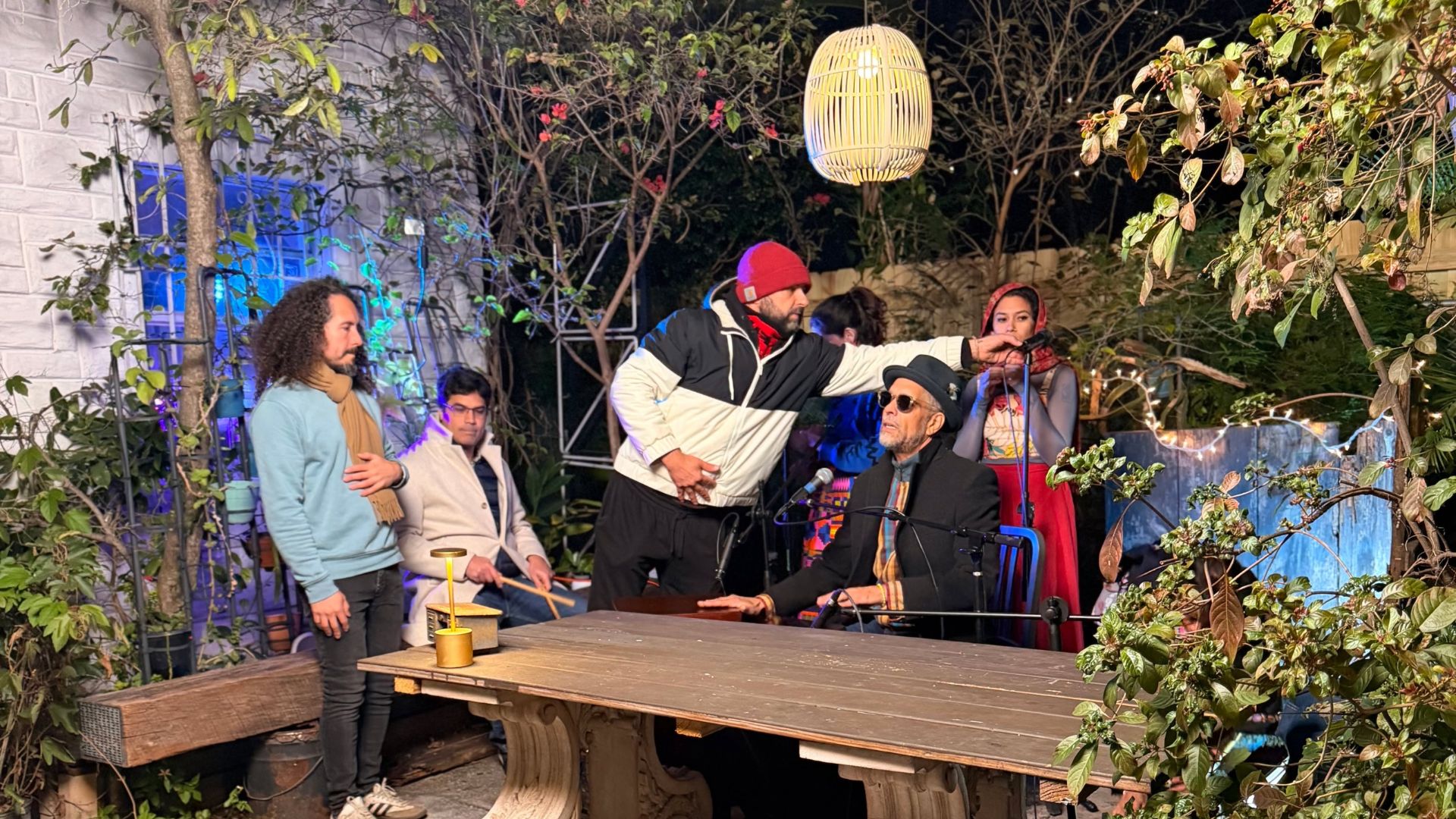 Photo of a band sitting by a table in a patio and a man holding a microphone