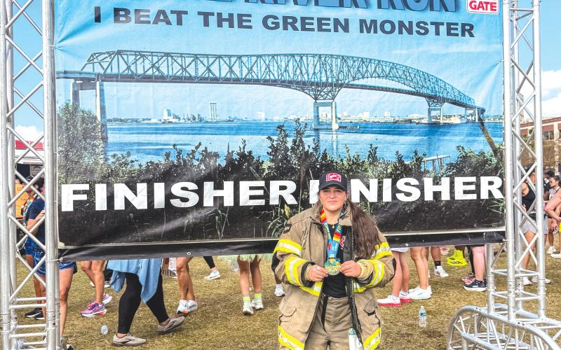 Christina Munro, a member of the Lake City Fire Department, holds her medal after finishing the Gate River Run in Jacksonville last week. Munro did the 15K run in her firefighting gear. (COURTESY)
