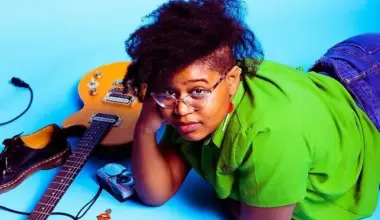 Woman laying propped on her arm next to a guitar on the floor.