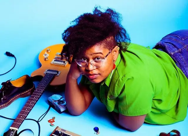 Woman laying propped on her arm next to a guitar on the floor.
