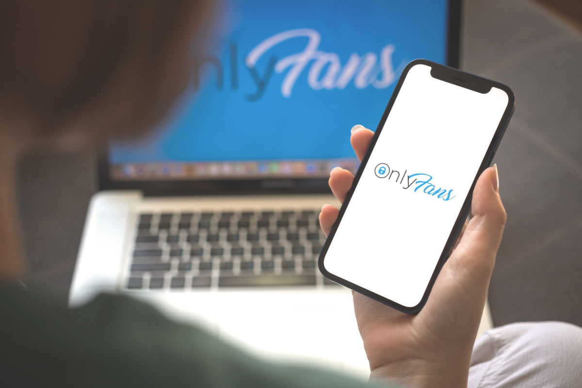 A photo of a phone with the "OnlyFans" logo on the screen alongside a laptop with the "OnlyFans" logo on the screen.