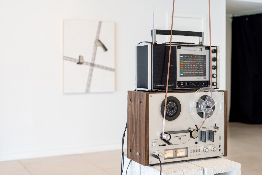 photo of a sculptural art piece depicting a radio stacked on top of a reel tape machine on a platform inside a gallery