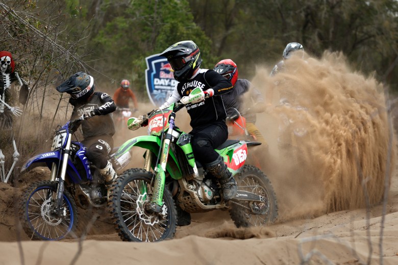 Several motocross riders racing dirt bikes on a sandy track, kicking up a massive cloud of dust